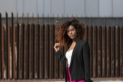 Young woman with curly hair standing against wall