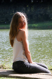 Portrait of young woman with long hair sitting against lake