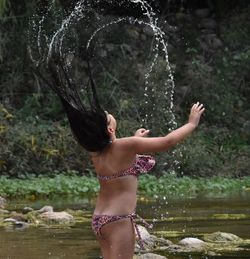 Rear view of woman tossing wet hair while standing in lake