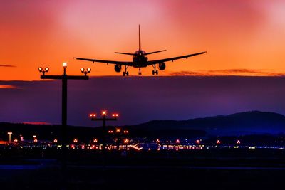 Airplane landing at airport against orange sky