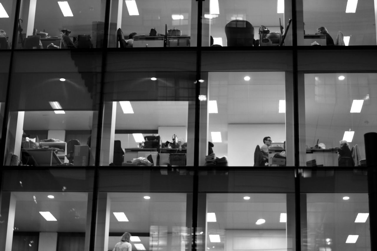 REFLECTION OF PEOPLE IN ILLUMINATED OFFICE BUILDING