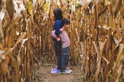 Brother and sister standing back to back amidst plants in agricultural field