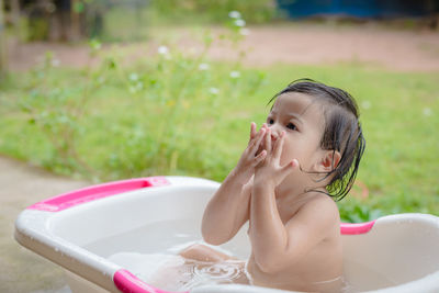 Cute baby girl looking away while sitting in bathtub at yard