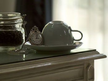 Close-up of pocket watch and cup on saucer