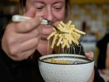 Woman, in blurry background, holding a fork with mac and cheese and a porcelain bowl.