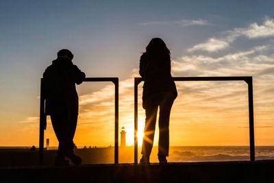 Silhouette of couple standing on sea at sunset