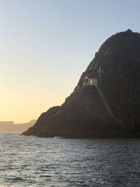 Scenic view of sea by mountain against clear sky