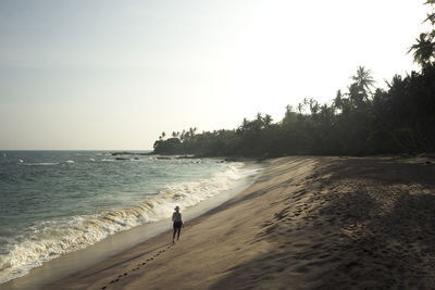 Rear view of young woman walking on shore at beach