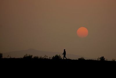 Silhouette man walking on landscape against sky during sunset