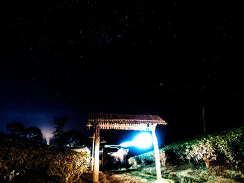 Illuminated lighting equipment on tree against sky at night