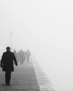 Rear view of people walking on footpath against sky