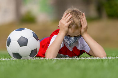 Boy wearing mask lying down with soccer ball on field