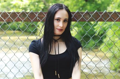 Portrait of beautiful woman standing against chainlink fence