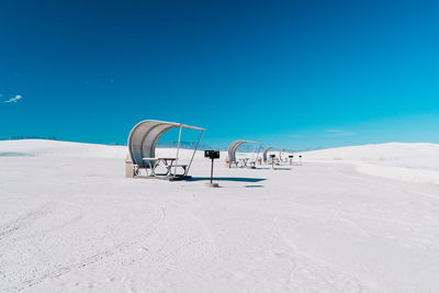 Picnic tables on sand against blue sky