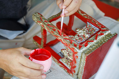 Close up a man's hand holding a brush is painting red on the altar table