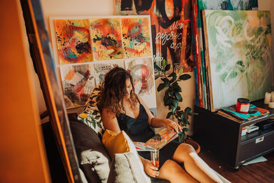 Artist sitting in home studio surrounded by canvas and paintings