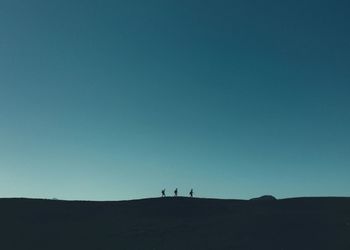 Silhouette people walking on desert against clear blue sky