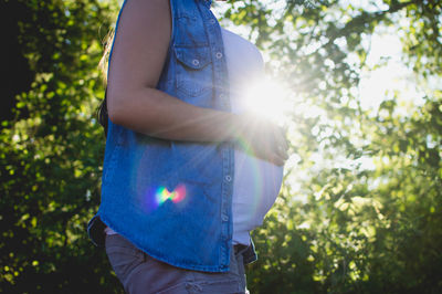 Midsection of woman standing on tree against sun