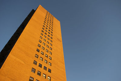 Low angle view of orange apartment building with thick shadow against clear blue sky.