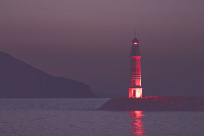 Lighthouse by sea against sky at night