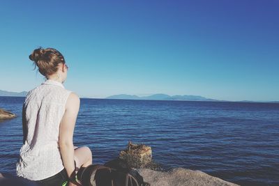 Rear view of woman sitting against sea at beach