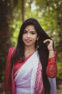 Portrait of beautiful young woman in sari standing against trees