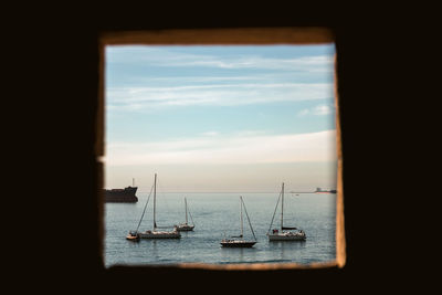 Sailboats sailing in sea against sky seen through window