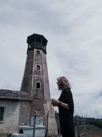 Side view of woman standing by lighthouse against sky