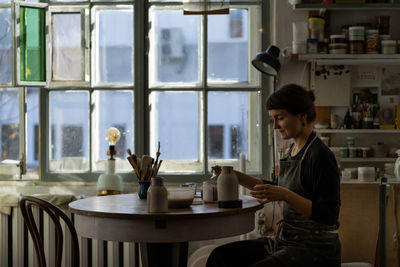 Young skilled lady concentrated on modeling jug from raw clay enjoys hobby creating vase