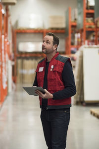 Salesman holding digital tablet while looking at shelf in hardware store