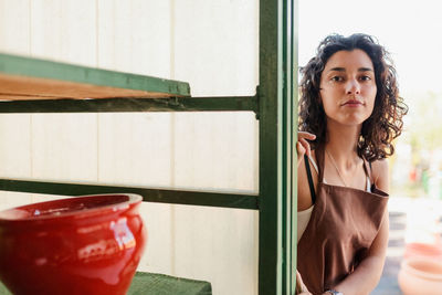 Portrait of beautiful young woman standing against window in pottery shop