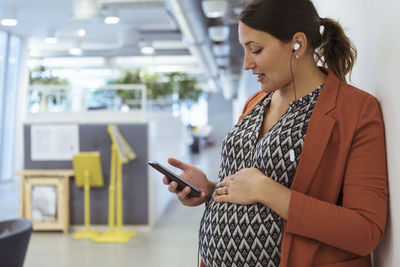 Pregnant businesswoman listening music on smart phone with hands on stomach at office
