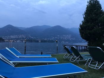 Empty chairs by swimming pool against sky