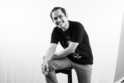 Portrait of young man sitting against wall