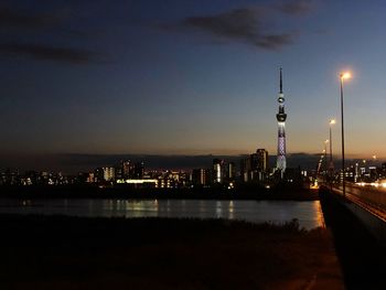 Illuminated modern buildings by river against sky at night