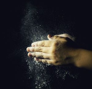 Close-up of hands spraying powder over black background