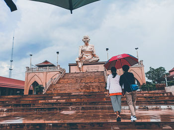 Low angle view of woman standing by statue against sky