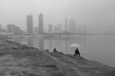 People on sea by buildings against sky during rainy season