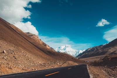 Road leading towards mountains against blue sky