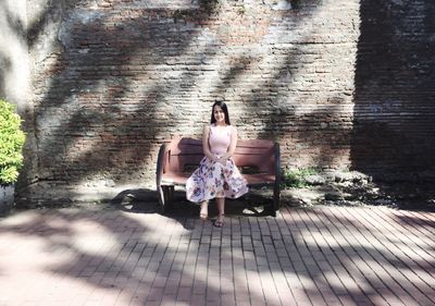 Portrait of beautiful woman sitting on bench against brick wall