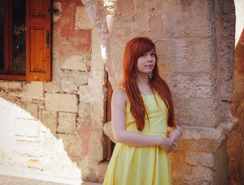 Portrait of young woman standing against brick wall