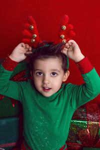 Baby boy in a green t shirt and with deer antlers sits with gifts on a red background