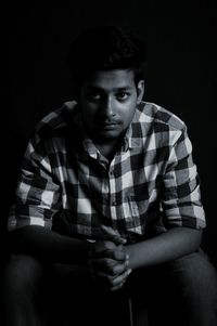Portrait of young man sitting against black background