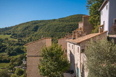 Houses and trees by mountains against clear blue sky