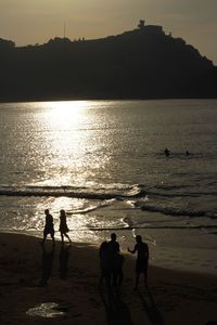 Silhouette people on beach against sky during sunset