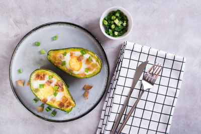 Baked avocado with egg, bacon and chives on a plate on the table for a keto diet top view