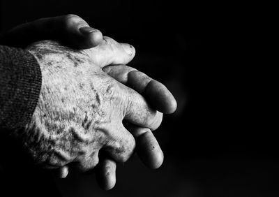 Cropped image of person with hands clasped against black background