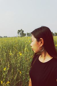 Side view of young woman standing on field against sky