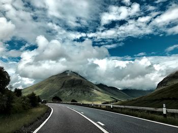 Empty road by mountains against sky