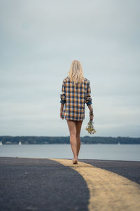 Rear view of woman holding flowers while walking on road